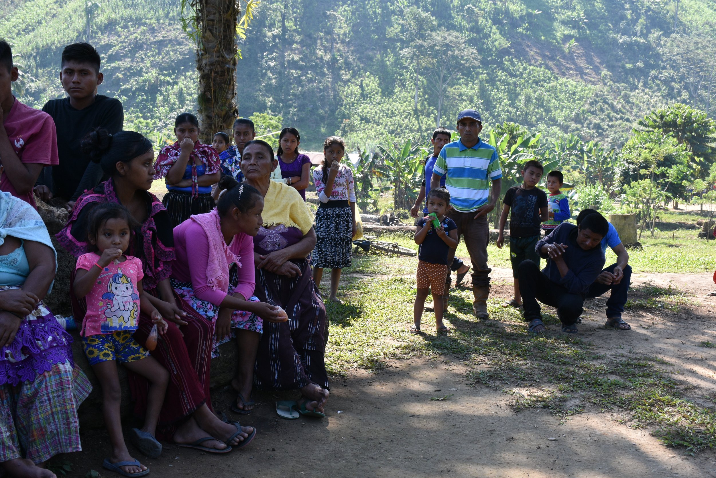  Mujeres, niñas, niños y hombres de Palestina Chinebal reunidos en el centro de la comunidad. Al fondo se observan las montañas en donde se desplazaron por los desalojos. Foto: Ketzali Pérez.  
